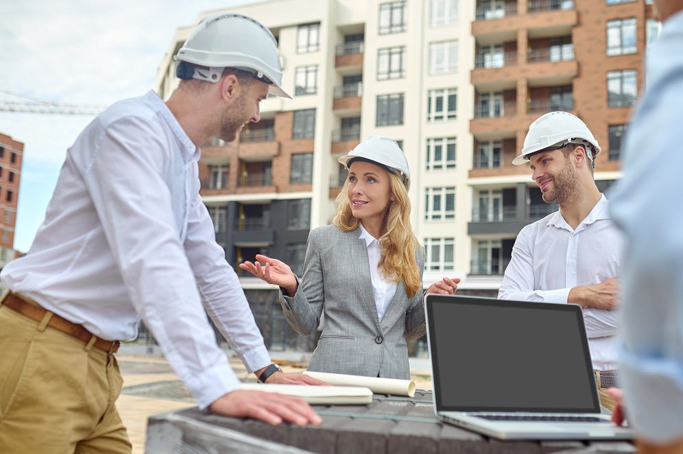 Attractive elegant middle-aged Caucasian female inspector standing on the construction site surrounded by three workers