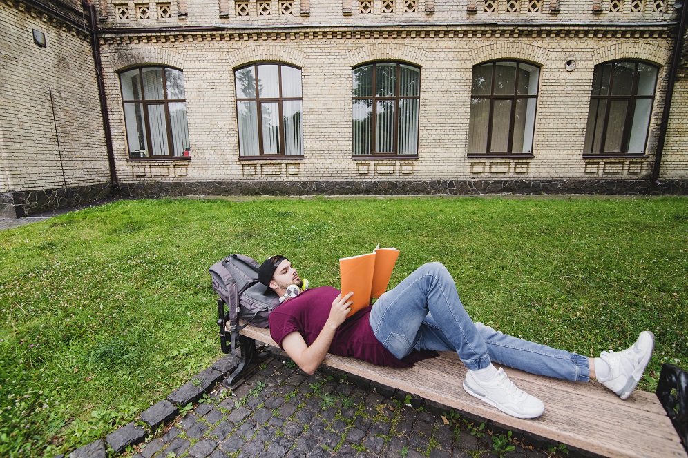 man-lying-wooden-bench-reading